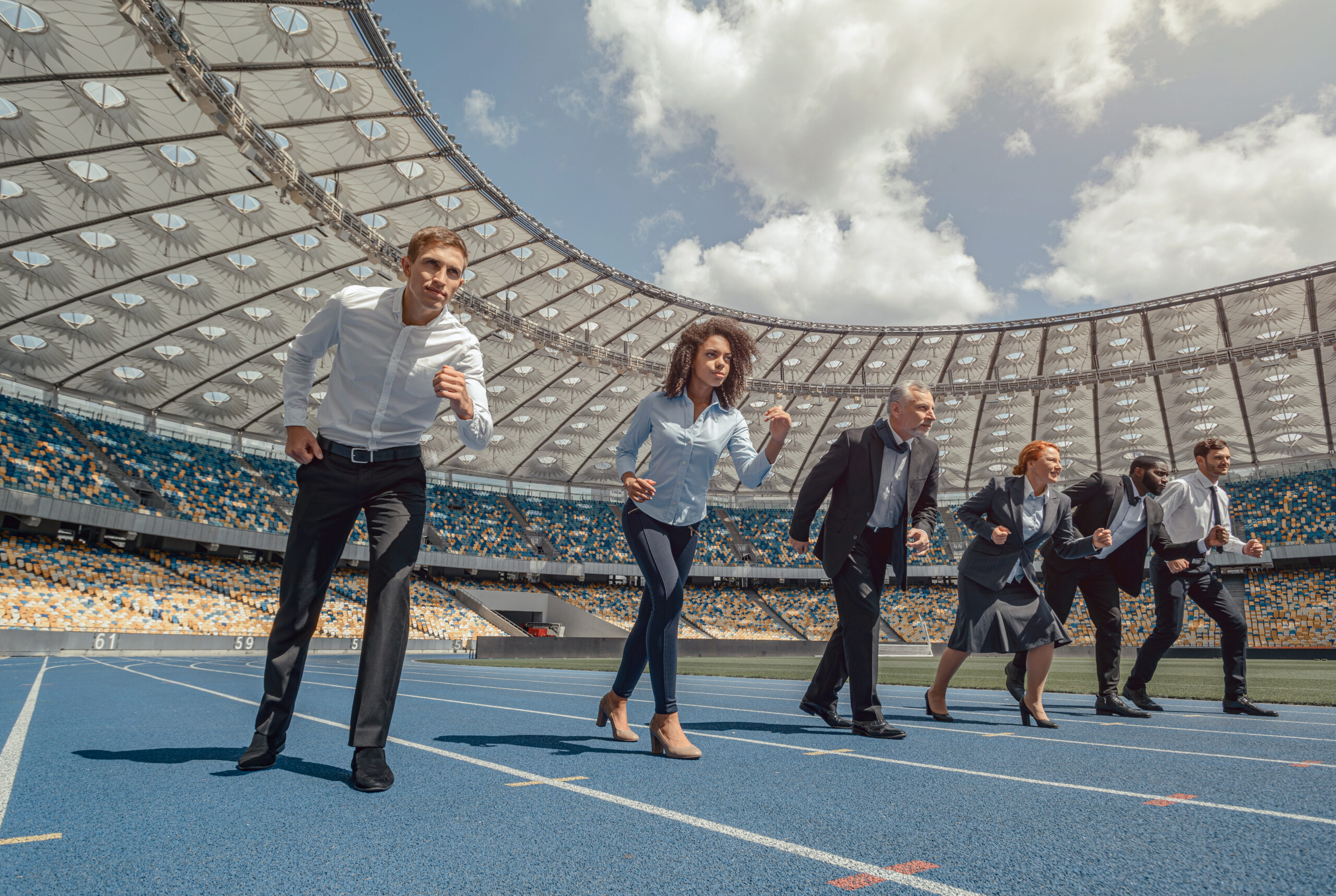 Multiracial business males and females competing in race on modern sport track, running to finish line